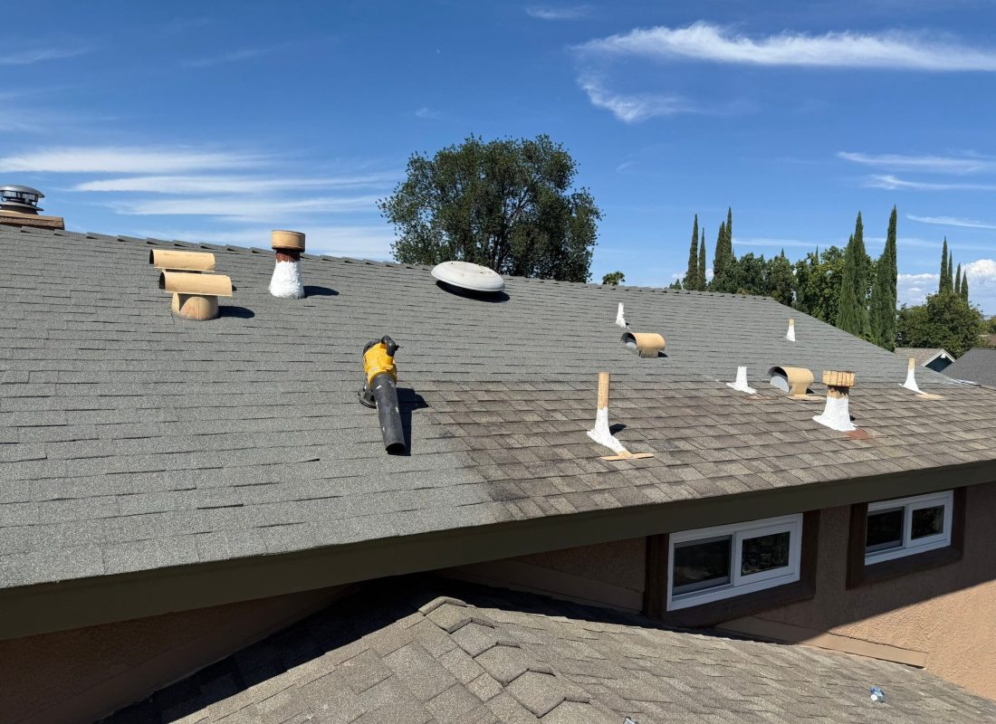 Roofing technician repairing shingles on a luxury Beverly Hills home under clear blue skies