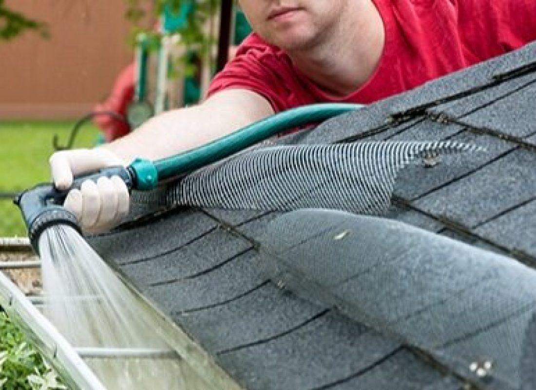 Specialist safely removing debris from commercial gutter system using harness and professional tools